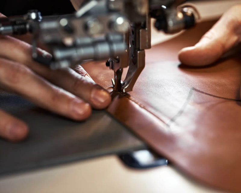 Close-up of hands using a sewing machine on leather.