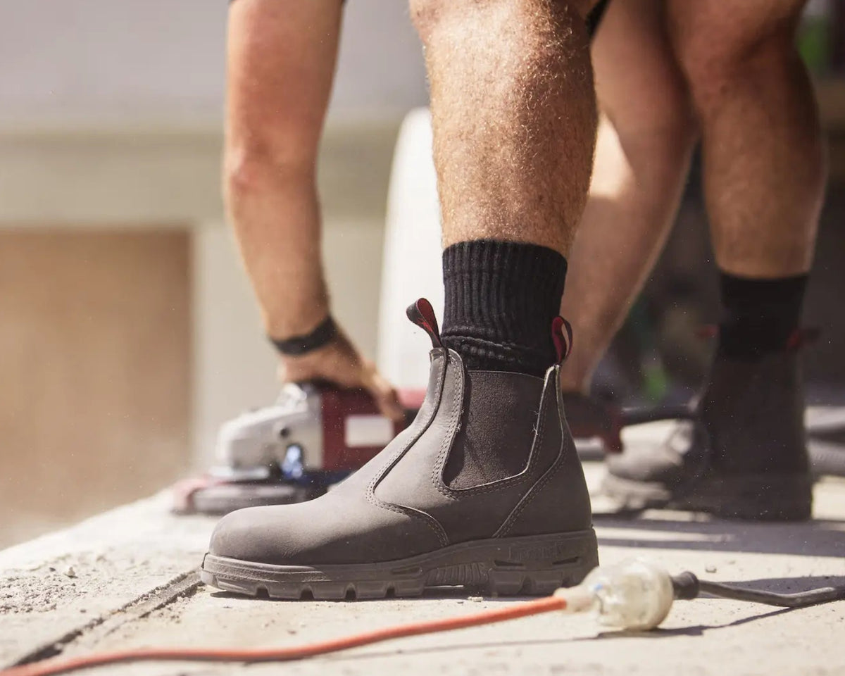 Person wearing dark brown bobcat chelsea boots boot while working