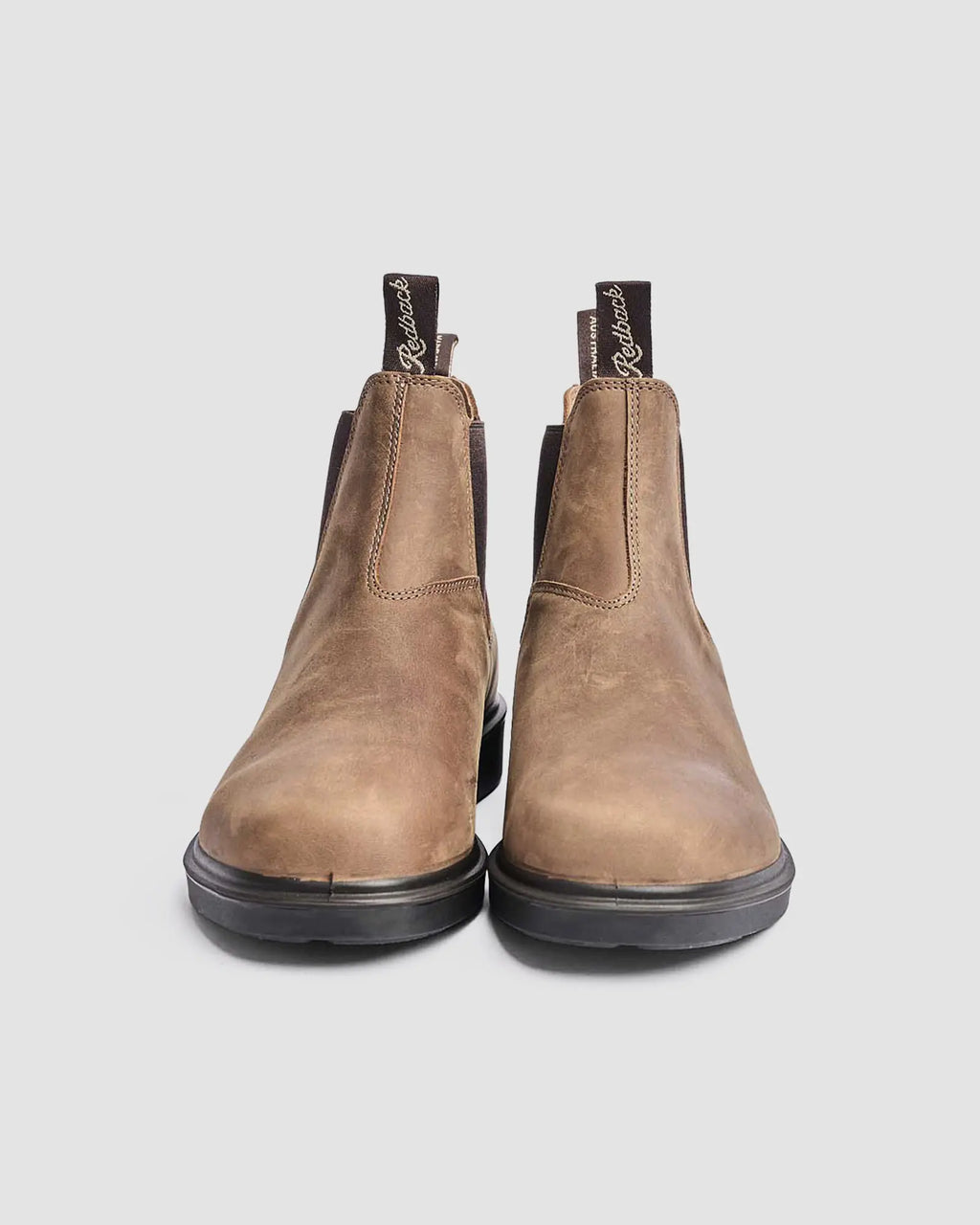 Pair of brown leather chelsea lifestyle boots with black soles on a light gray background